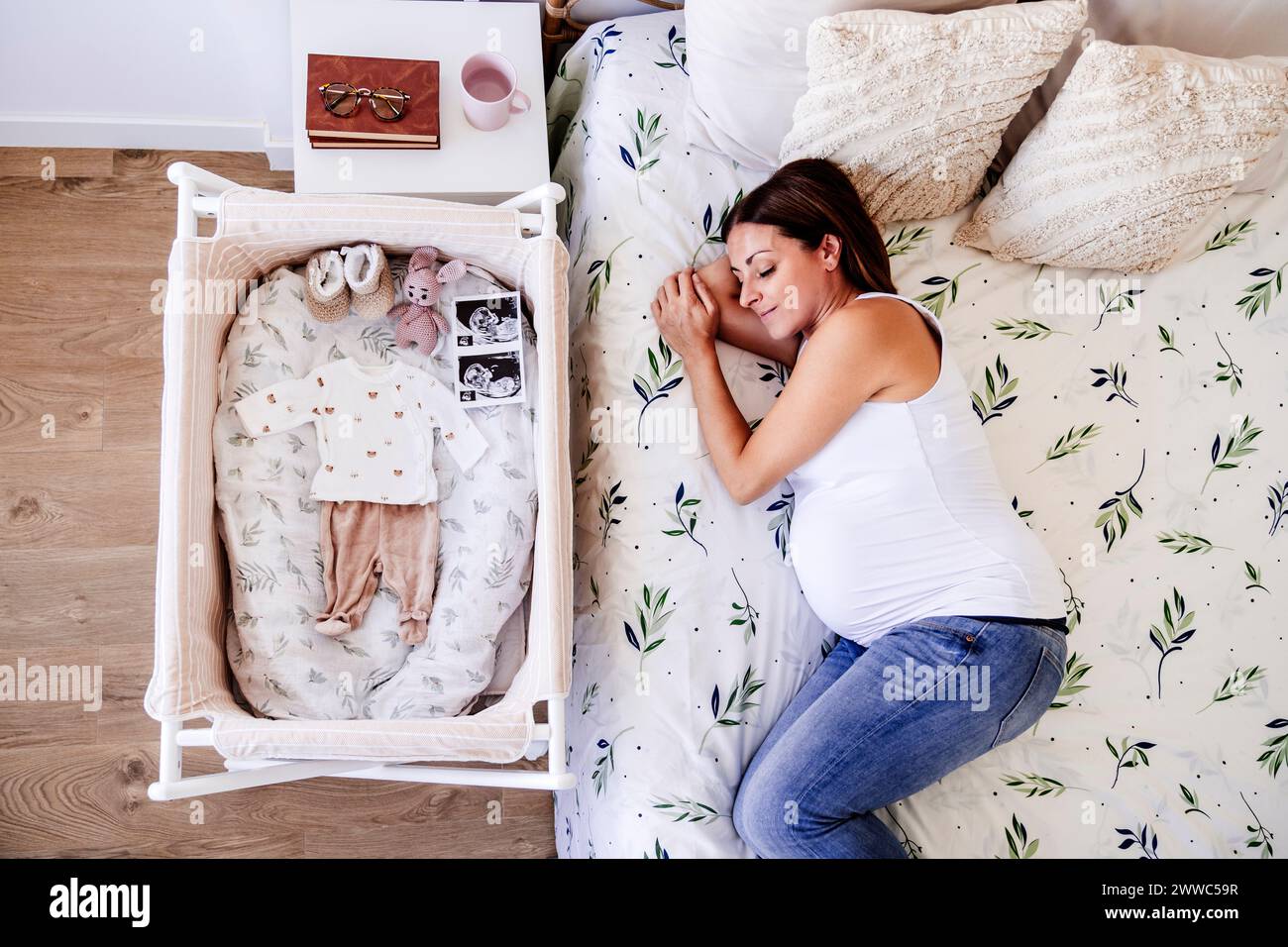 Donna incinta che dorme sul letto vicino alla culla di casa Foto Stock
