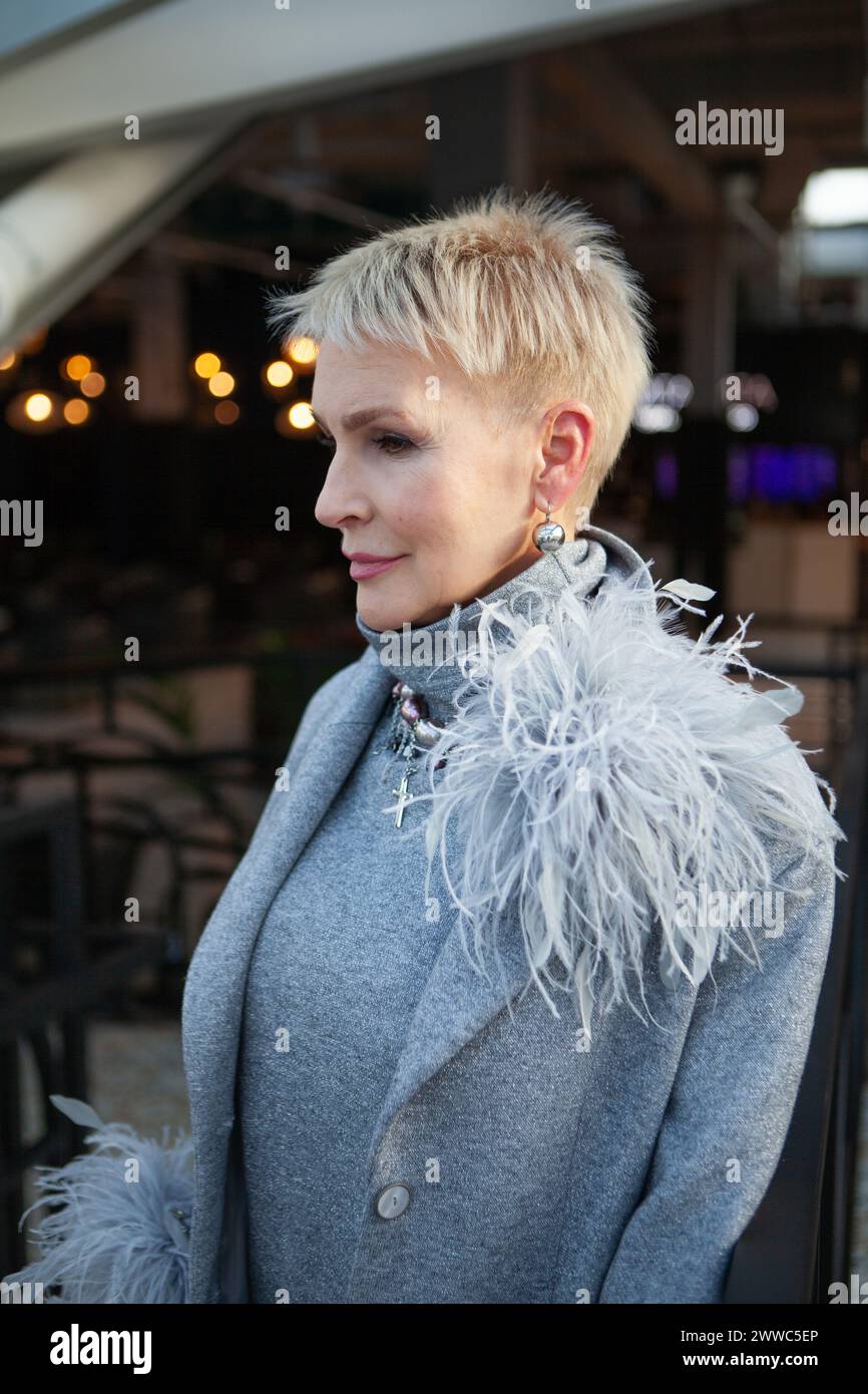 Ritratto di una donna matura con un taglio di capelli corto, vestito con una tuta grigia piuma e accessori alla moda, che mostra una tendenza alla moda Foto Stock