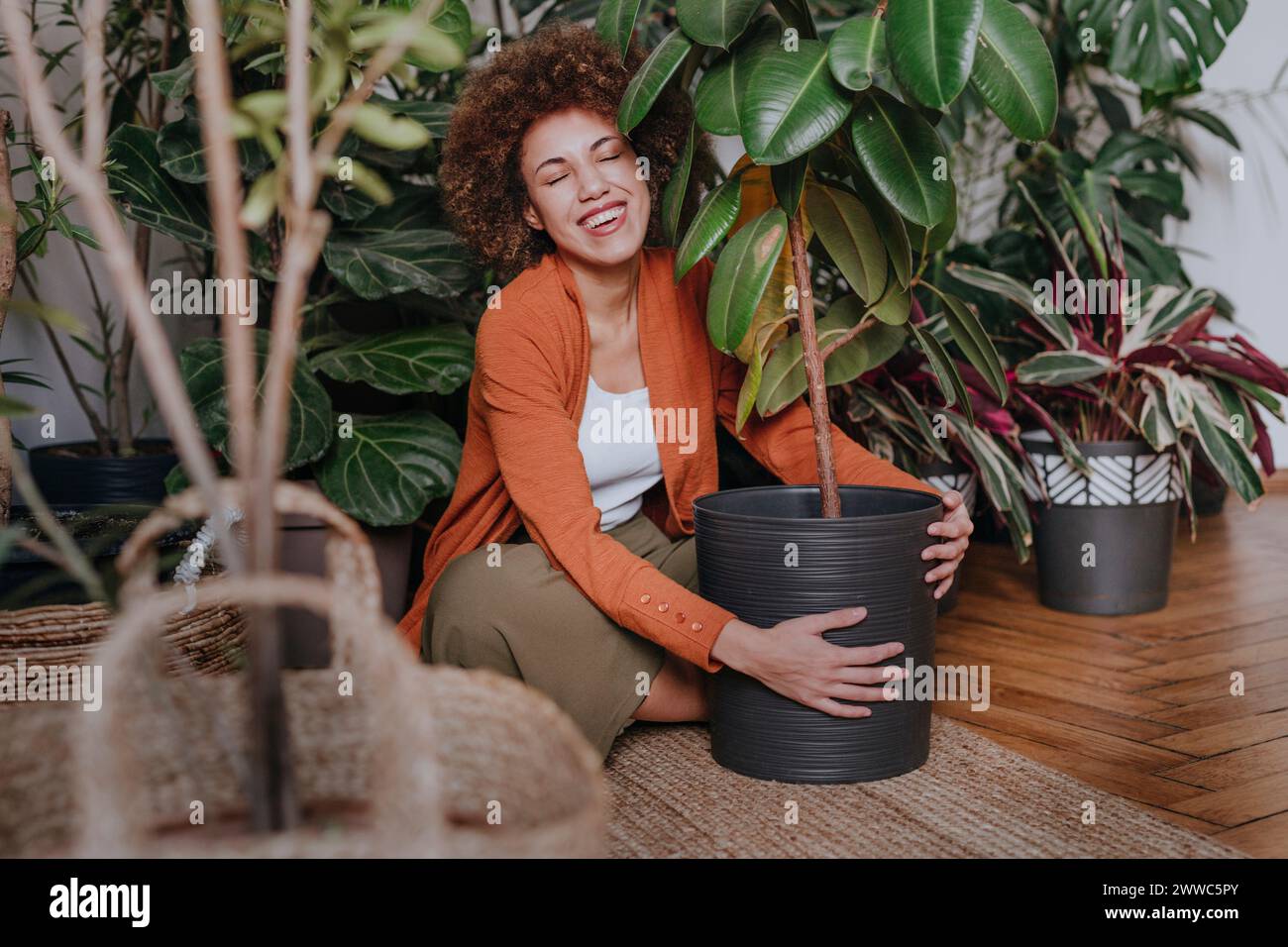 Donna felice seduta con piante su tappeto Foto Stock