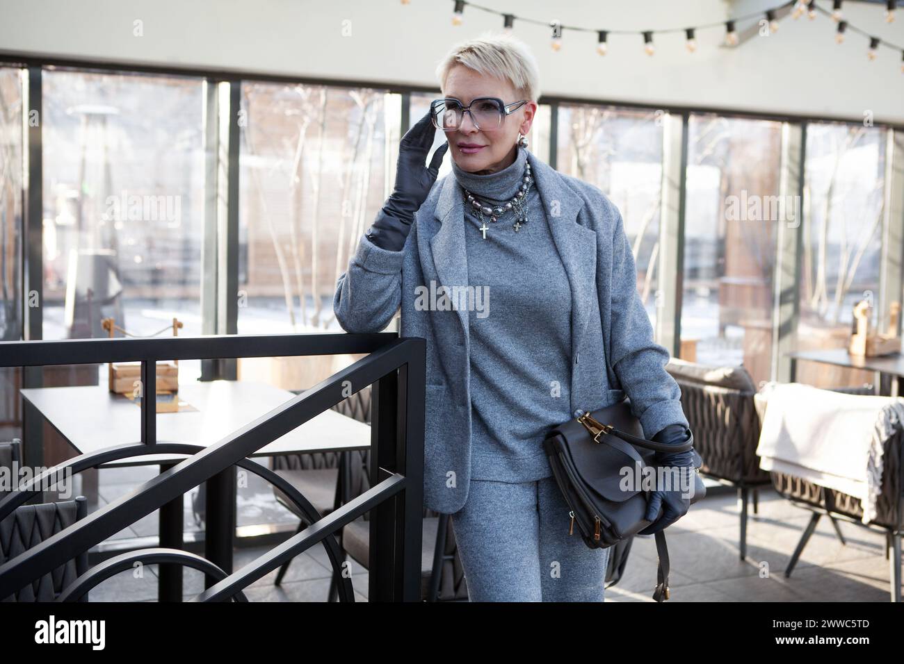 Donna matura attraente ed elegante in pantalone grigio con giacca e dolcevita, accessoriato con borsa. Il look perfetto per donne di successo Foto Stock