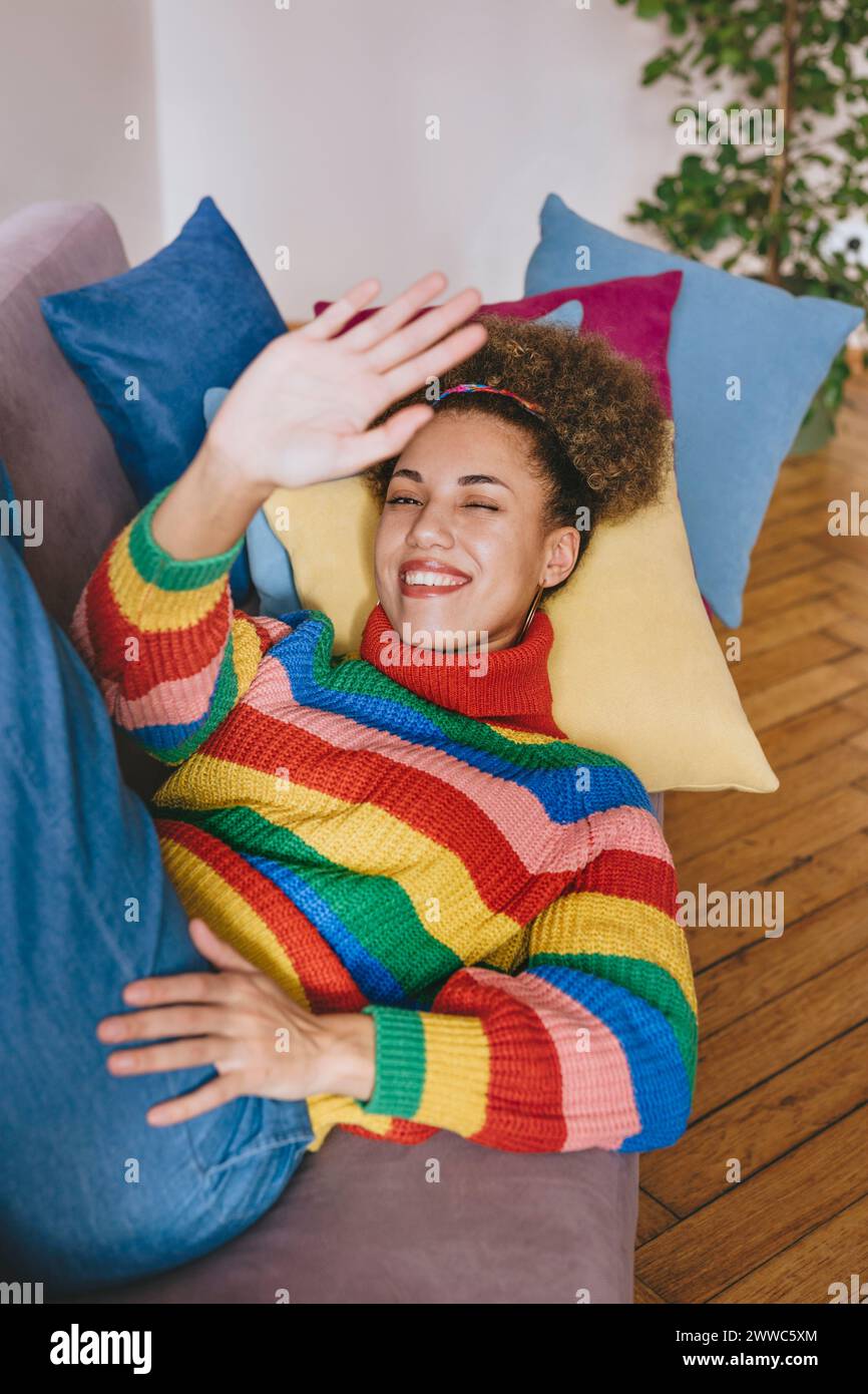 Donna sorridente che protegge gli occhi sul divano di casa Foto Stock