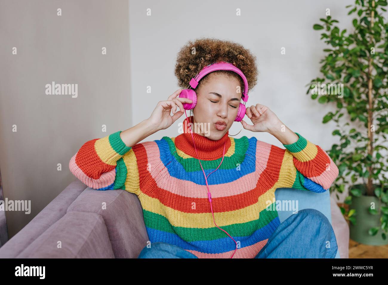 Giovane donna felice che ascolta la musica attraverso le cuffie a casa Foto Stock