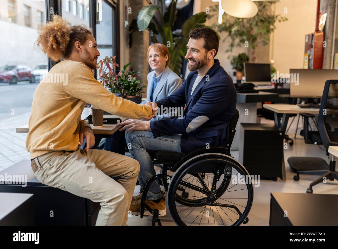 Uomo d'affari in sedia a rotelle che stringe la mano con il collega nello spazio di co-working Foto Stock