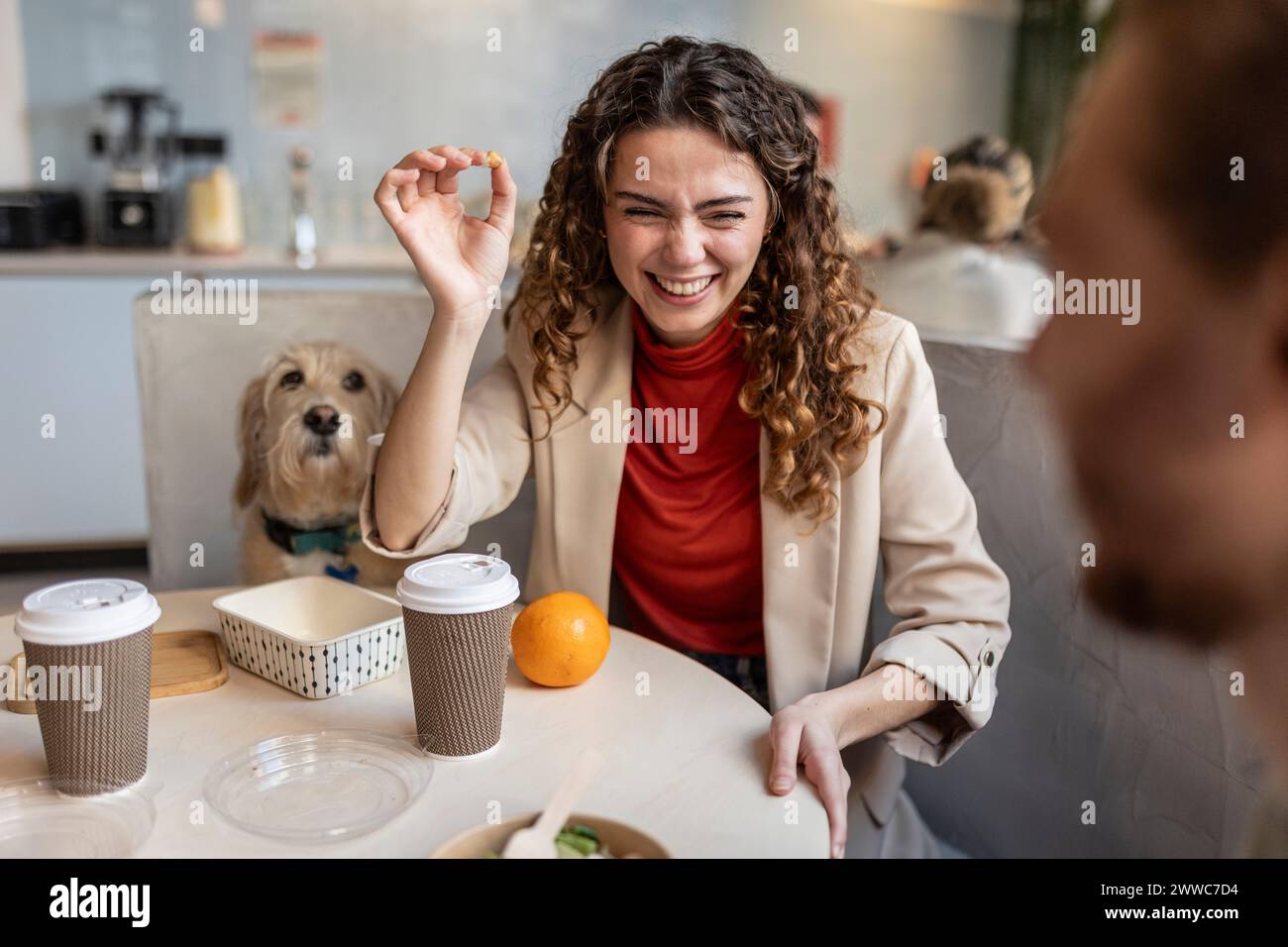 Donna d'affari felice che lancia cibo e collega seduta al bar dell'ufficio Foto Stock