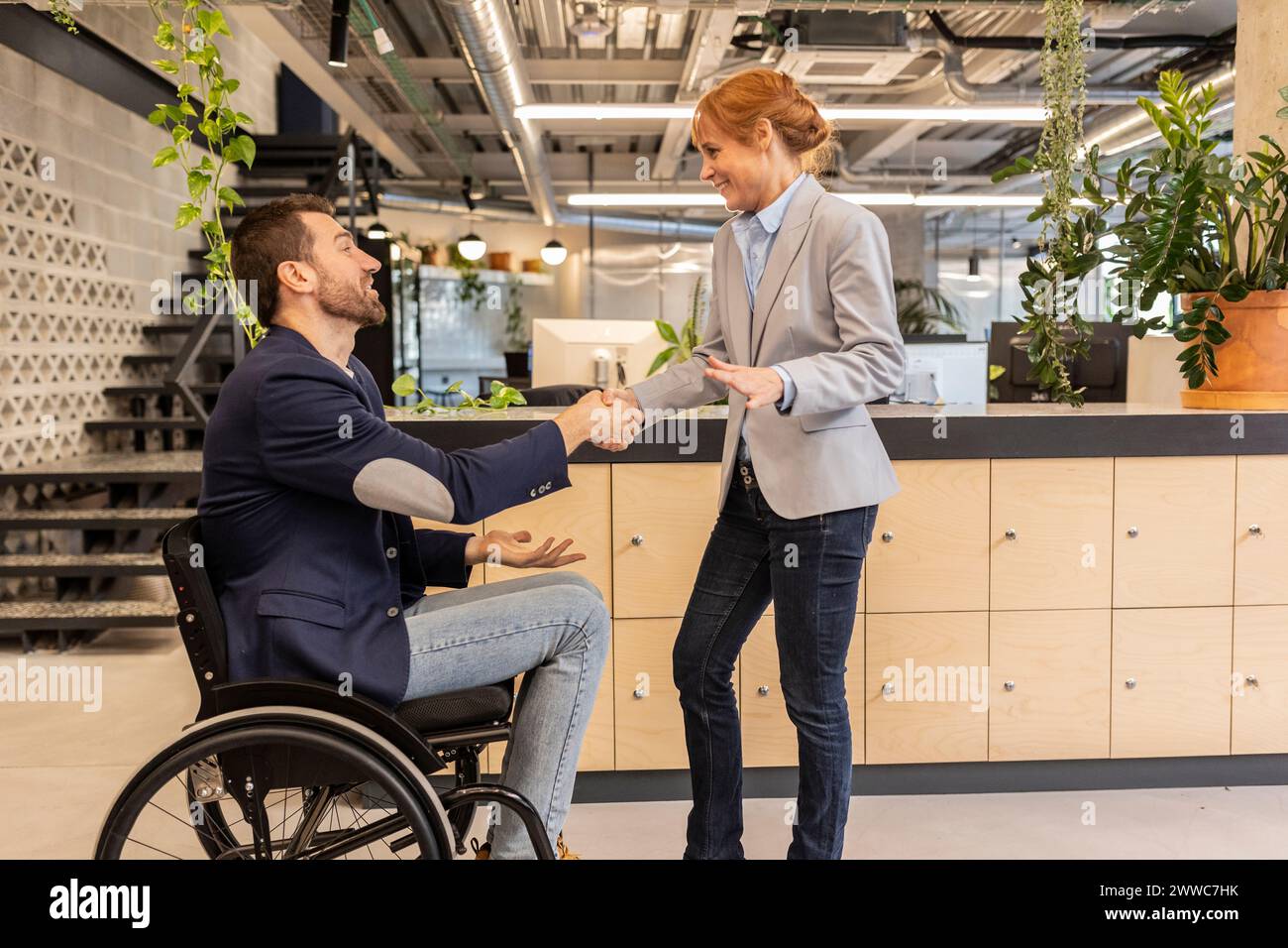 Il manager stringe la mano con il collega seduto in sedia a rotelle in ufficio Foto Stock