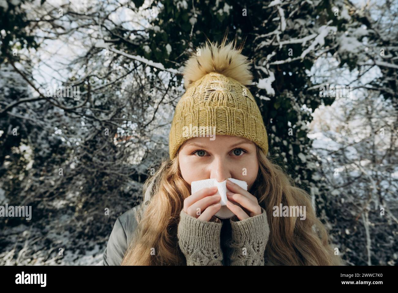 Donna che indossa un cappello in maglia e soffia il naso sui tessuti Foto Stock