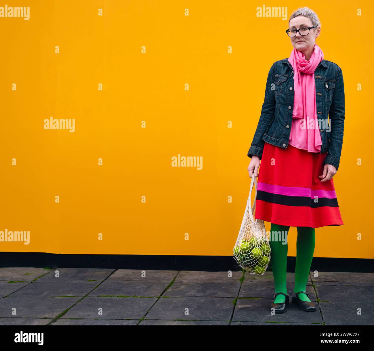 Donna matura che porta la spesa davanti al muro giallo Foto Stock