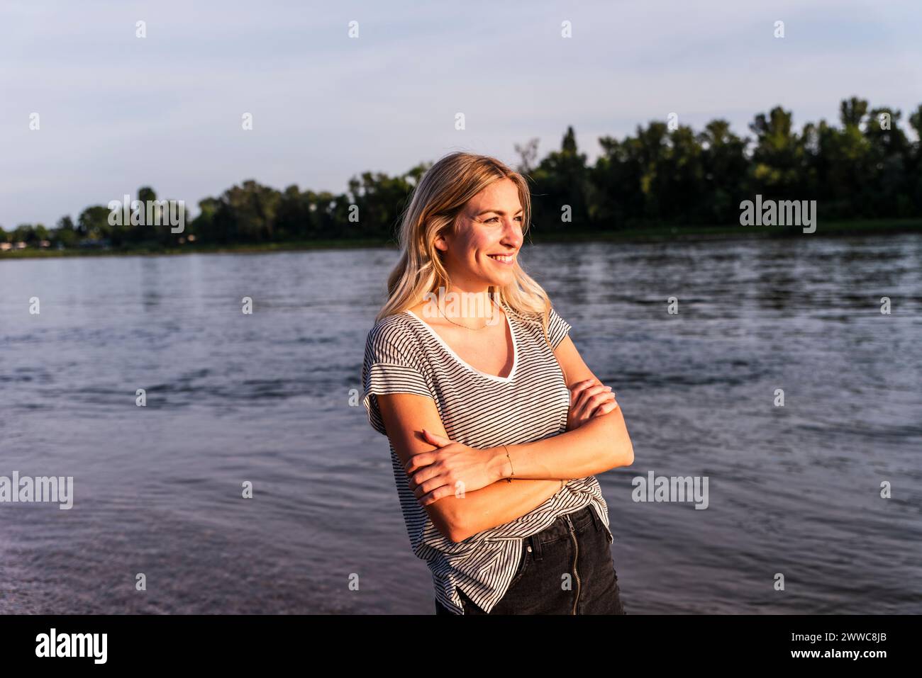 Donna felice in piedi con le braccia incrociate vicino al mare Foto Stock