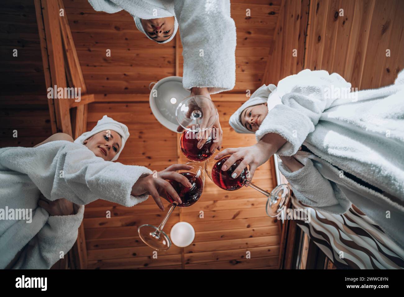 Amici che indossano accappatoi e tostano vino nella sauna Foto Stock