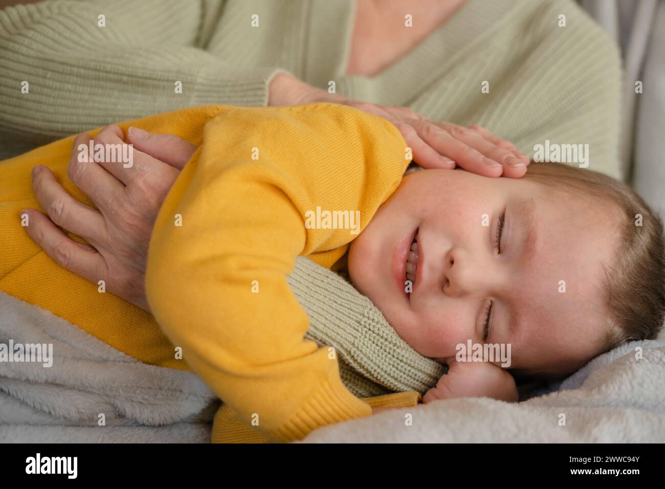 Ragazzo carino che dorme nel braccio della nonna a casa Foto Stock