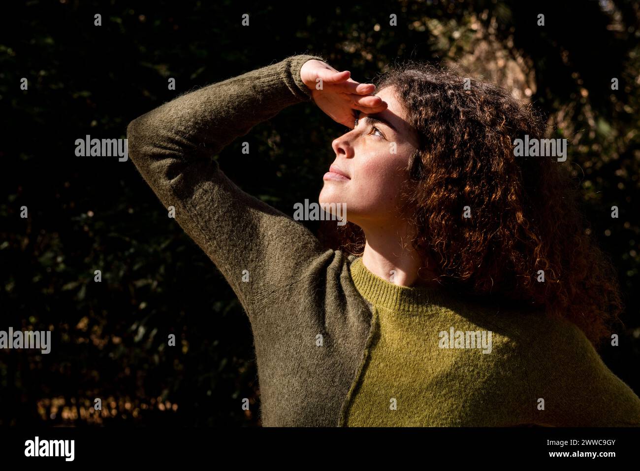 Giovane donna che protegge gli occhi dalla luce del sole al parco Foto Stock