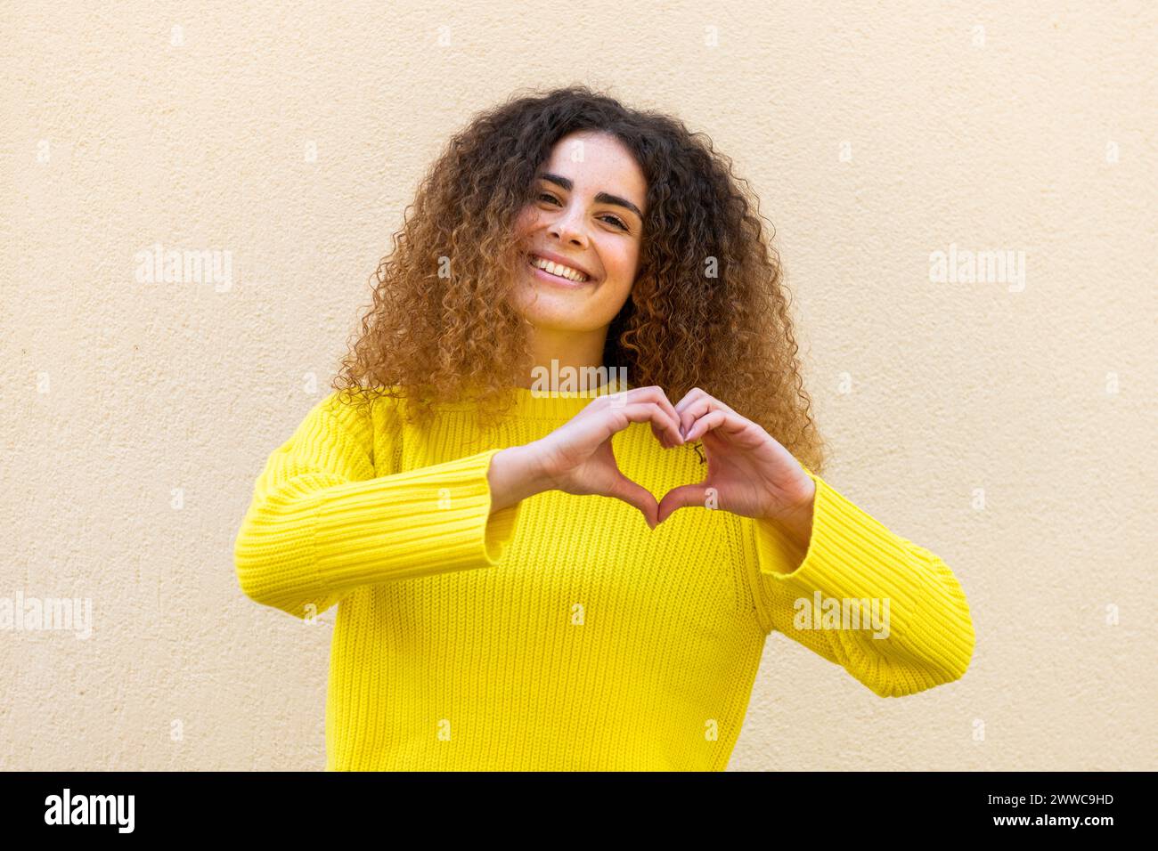 Donna felice che gestiva il cuore con le mani davanti al muro Foto Stock