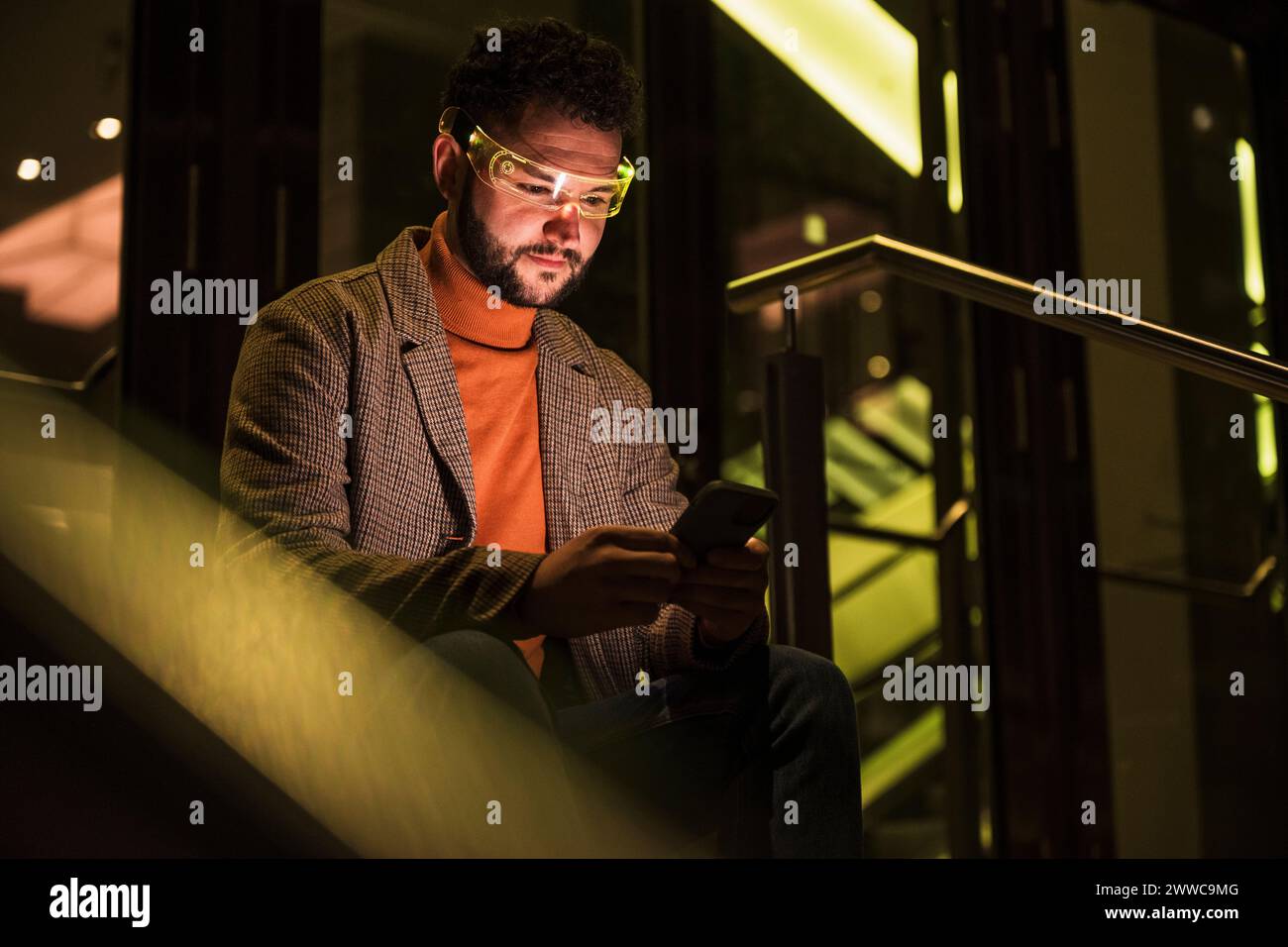 Uomo sorridente che indossa occhiali intelligenti e utilizza lo smartphone Foto Stock
