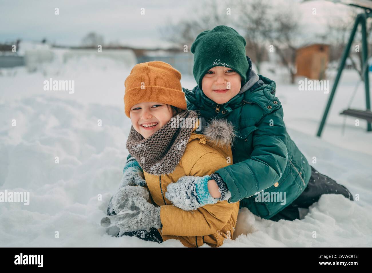 Fratelli felici che indossano abiti caldi e giocano sulla neve Foto Stock