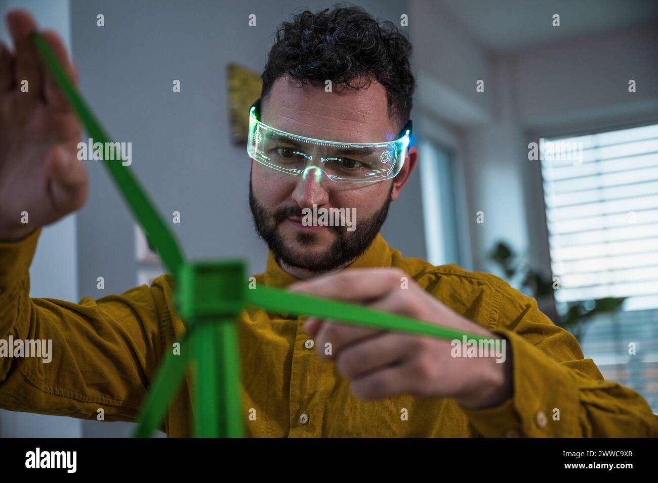 Architetto che indossa occhiali intelligenti ed esamina il modello di turbina eolica di colore verde Foto Stock Architetto che indossa occhiali intelligenti ed esamina il modello di turbina eolica di colore verde Foto Stock