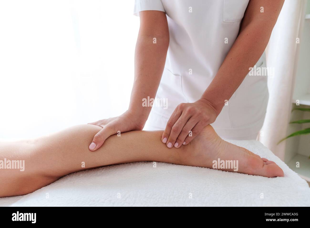 Osteopata che massaggia il polpaccio del paziente nella sala di trattamento Foto Stock