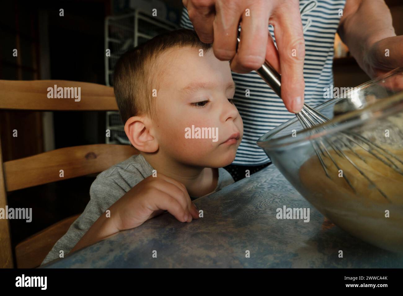 Curioso processo di apprendimento del nipote di mescolare l'impasto con la nonna a casa Foto Stock