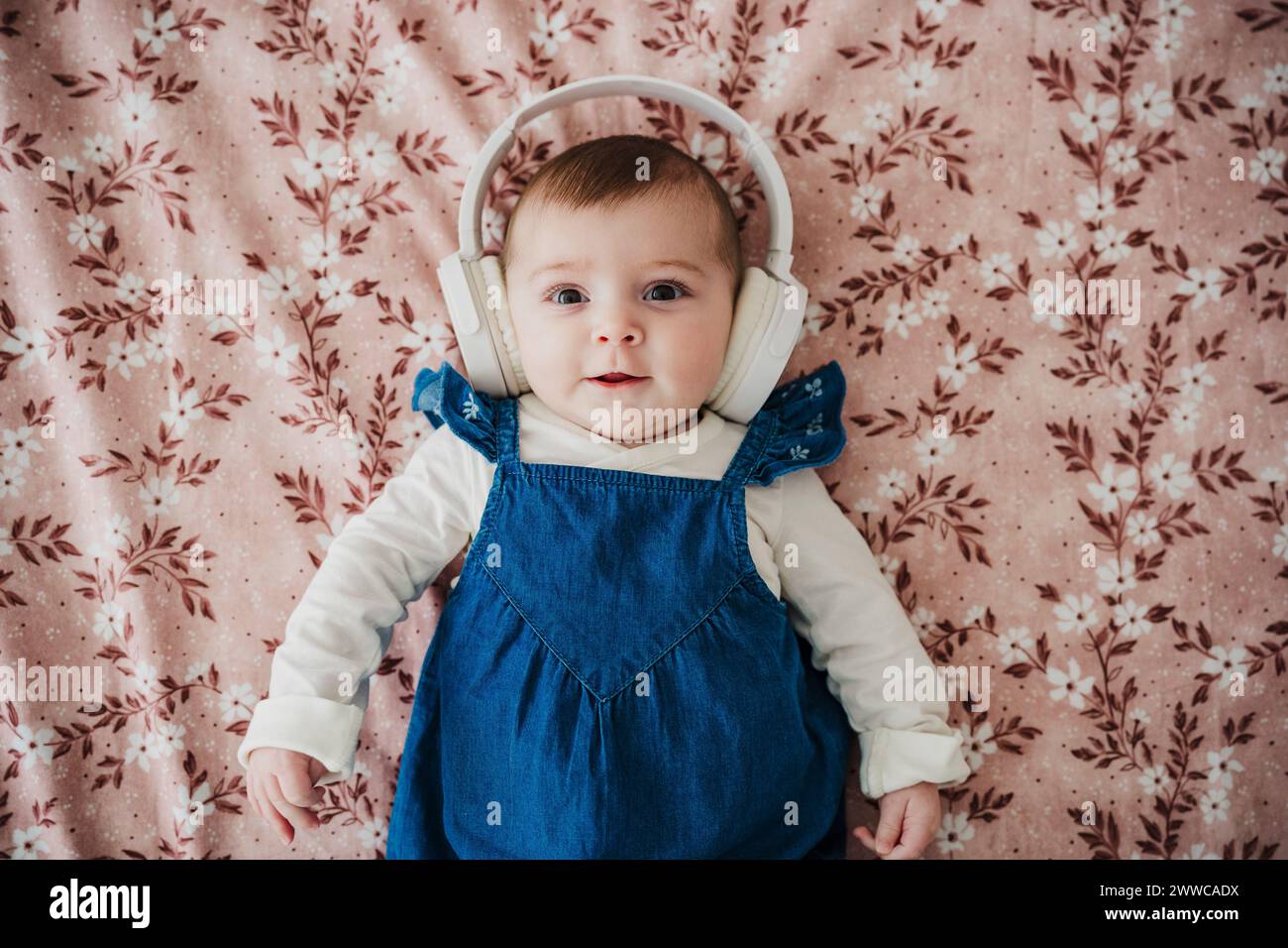 Una bambina simpatica che indossa cuffie wireless sdraiata sul letto di casa Foto Stock