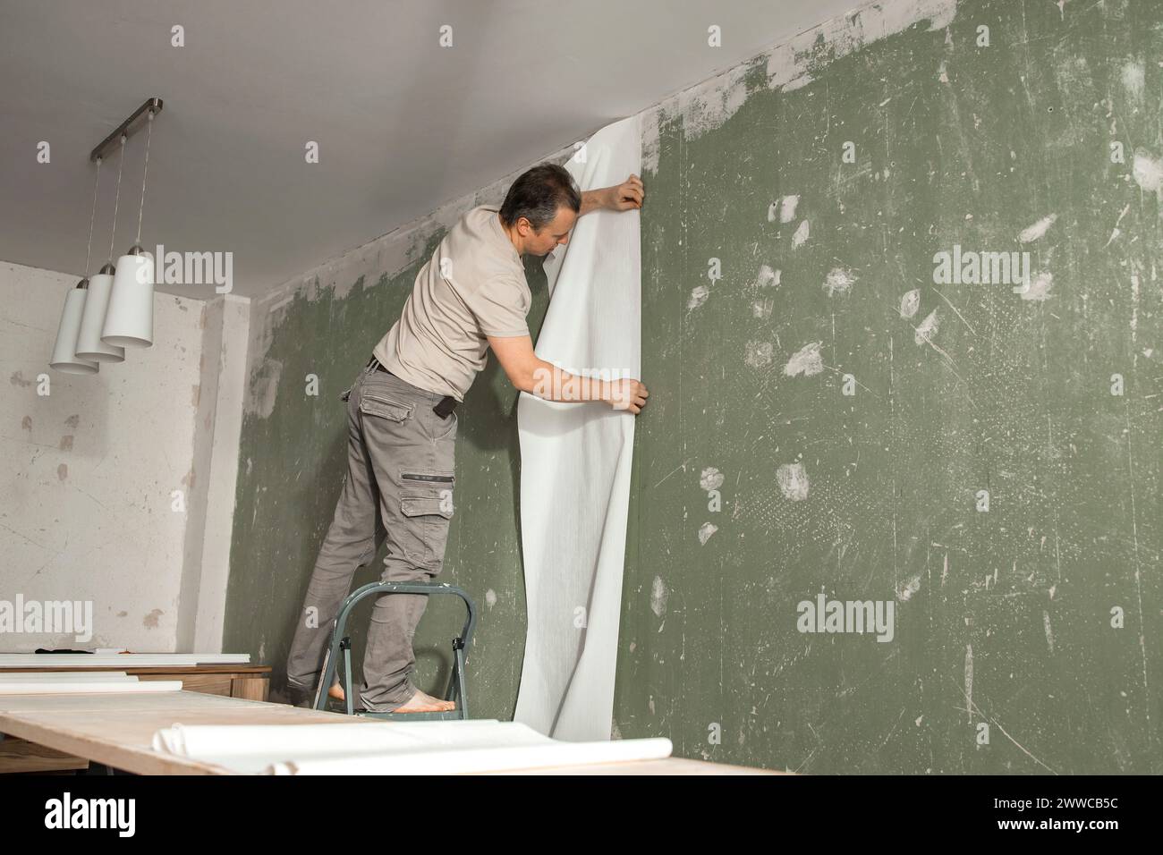 Uomo che incolla nuova carta da parati nel soggiorno di casa Foto Stock
