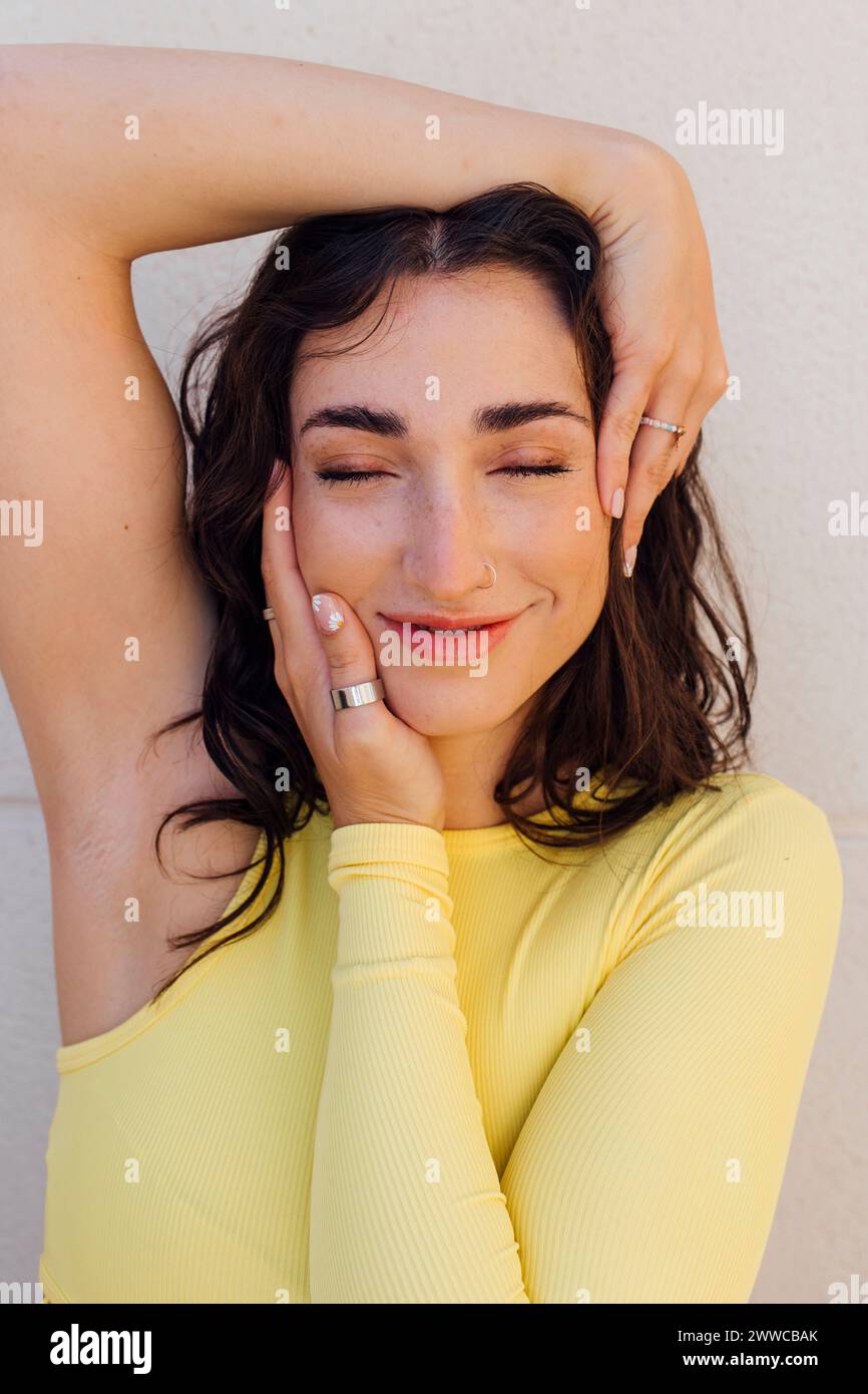 Donna sorridente con gli occhi chiusi su sfondo bianco che le toccano il viso Foto Stock