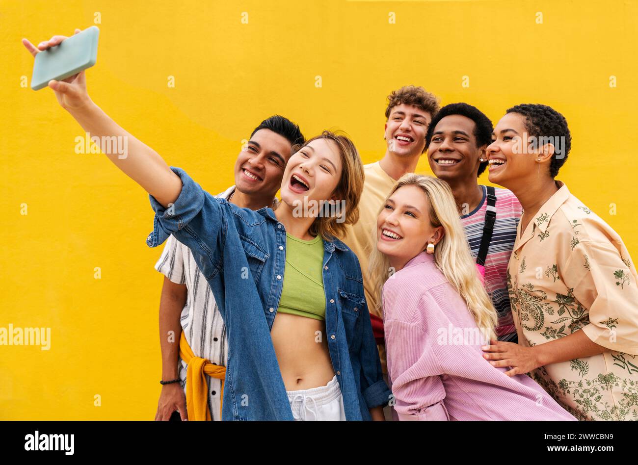 Lughing amici multietnici che scattano selfie su smartphone davanti al muro giallo Foto Stock