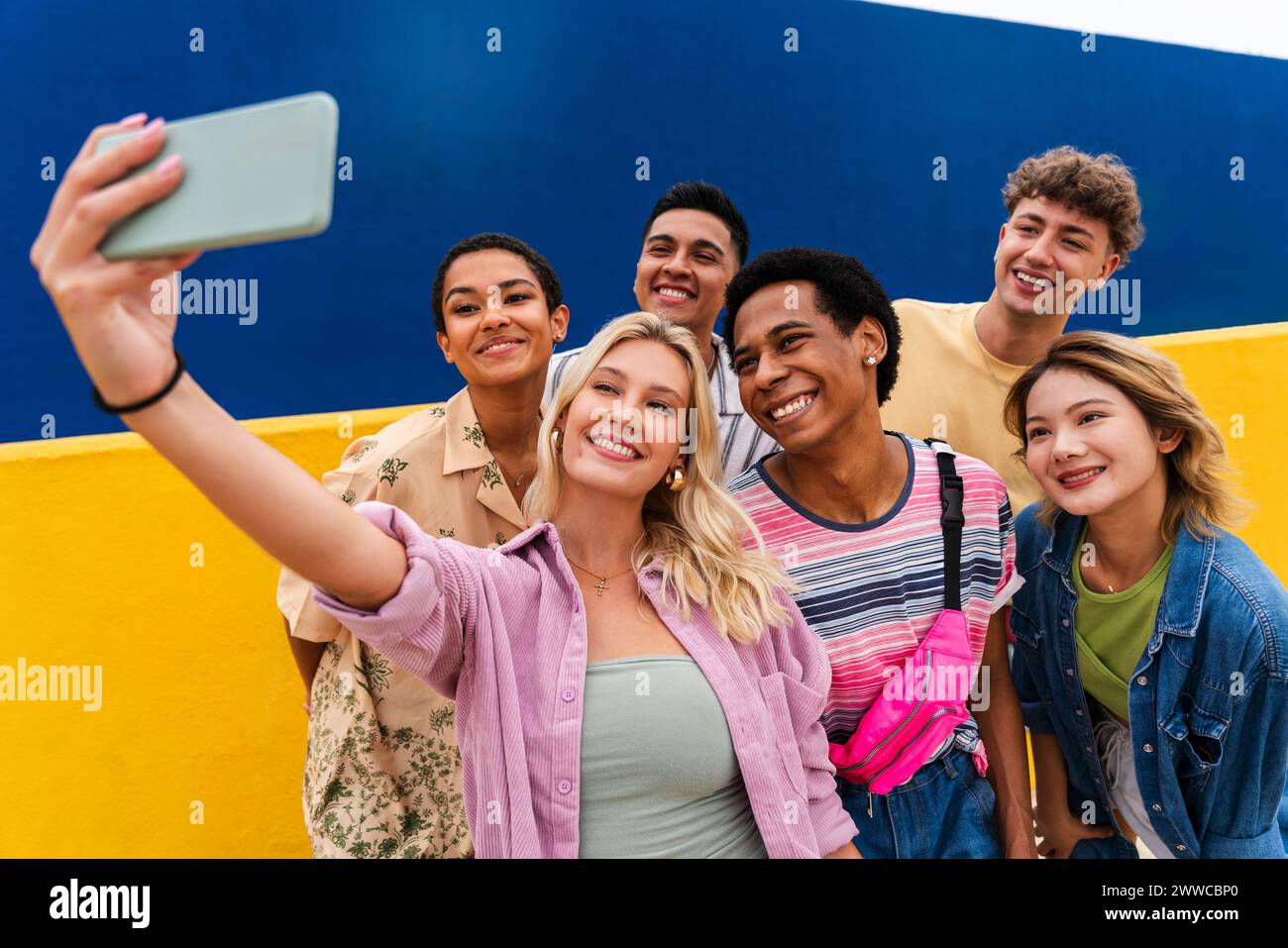 Amici multietnici che ridono scattando selfie su smartphone davanti al muro giallo Foto Stock
