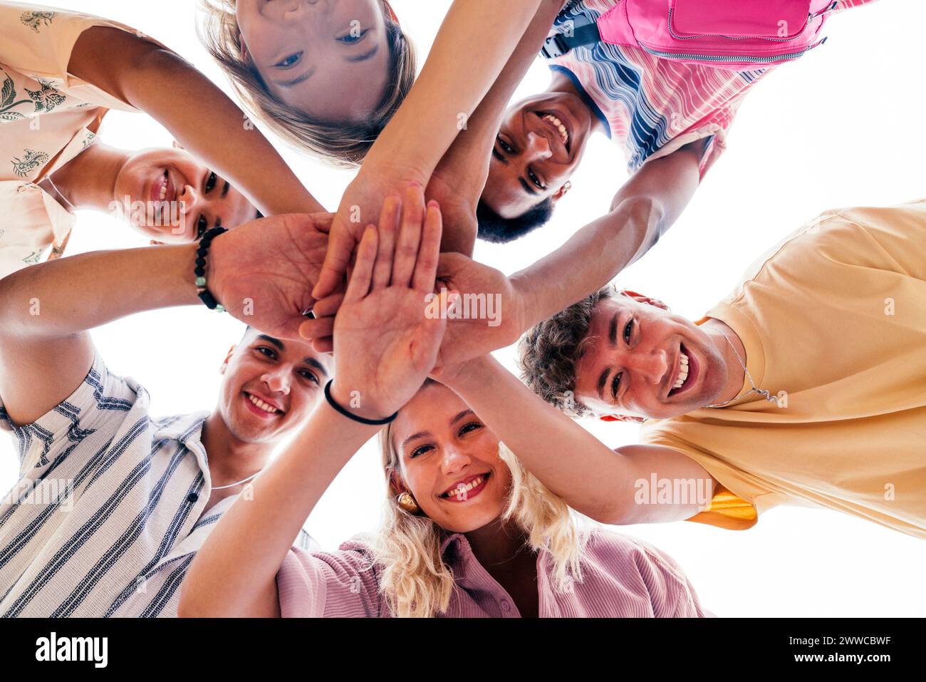 Un gruppo multietnico di giovani amici che stringono le mani che guardano verso il basso la fotocamera Foto Stock