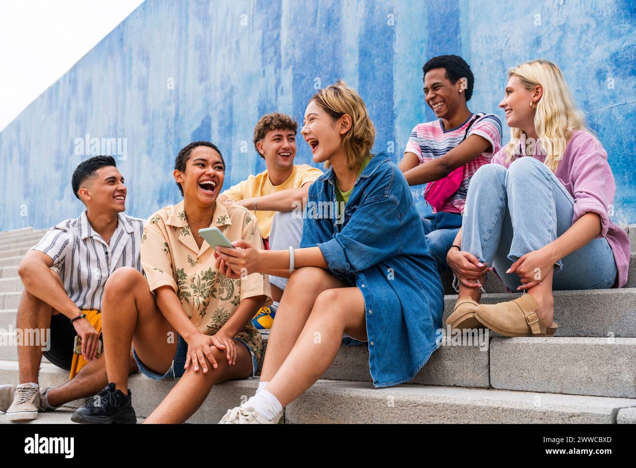 Gruppo felice di giovani che ridono sui gradini di fronte al muro Foto Stock
