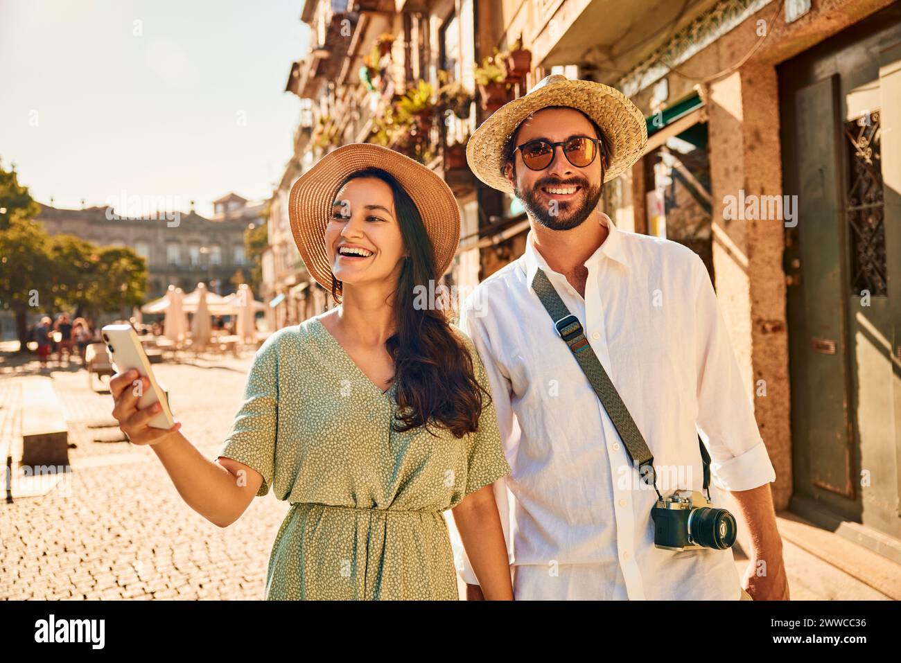 Donna felice che tiene uno smartphone con un uomo in strada vicino agli edifici Foto Stock Donna felice che tiene uno smartphone con un uomo in strada vicino agli edifici Foto Stock