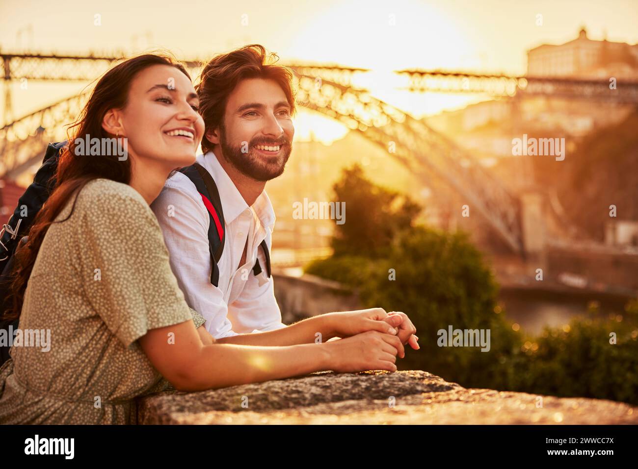 Coppia sorridente che si tiene per mano e si trova di fronte al ponte Dom Luis al tramonto, Porto, Portogallo Foto Stock Coppia sorridente che si tiene per mano e si trova di fronte al ponte Dom Luis al tramonto, Porto, Portogallo Foto Stock
