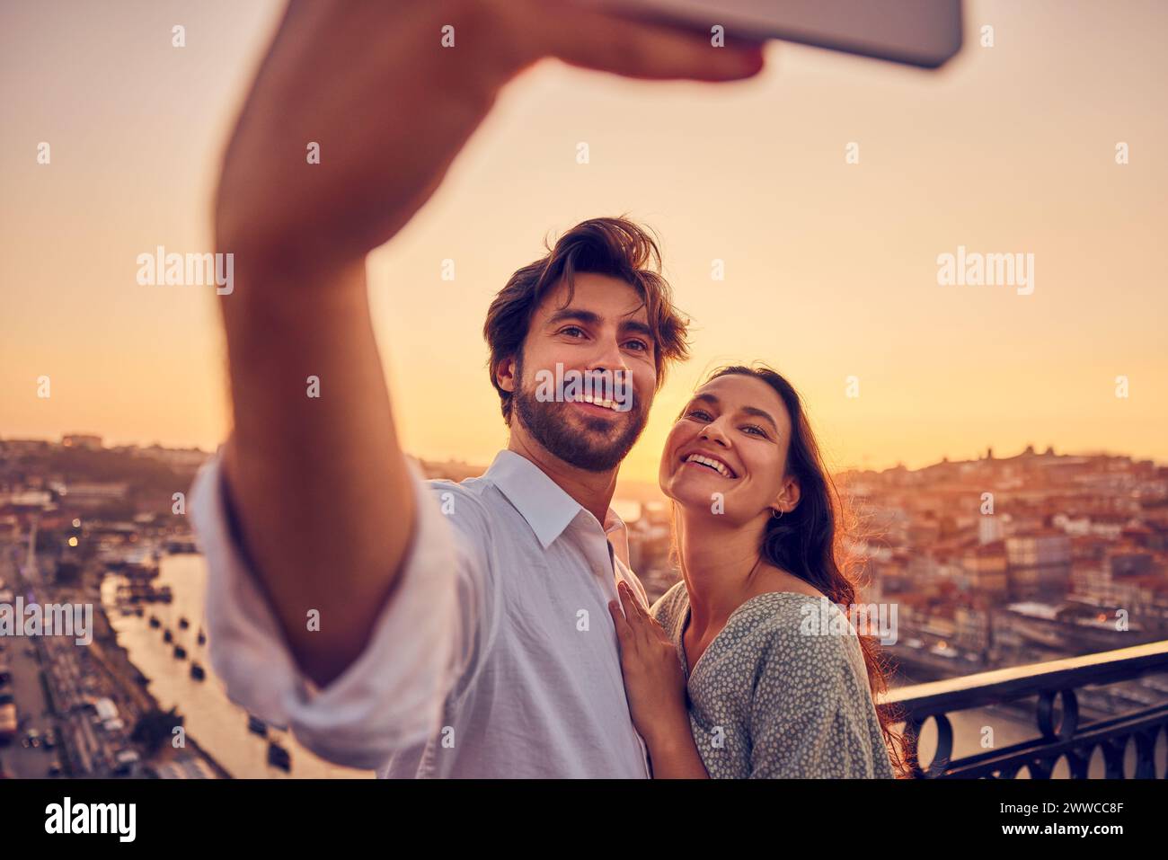 Coppia felice che scatta selfie tramite smartphone di fronte alla città di Porto al tramonto, in Portogallo Foto Stock