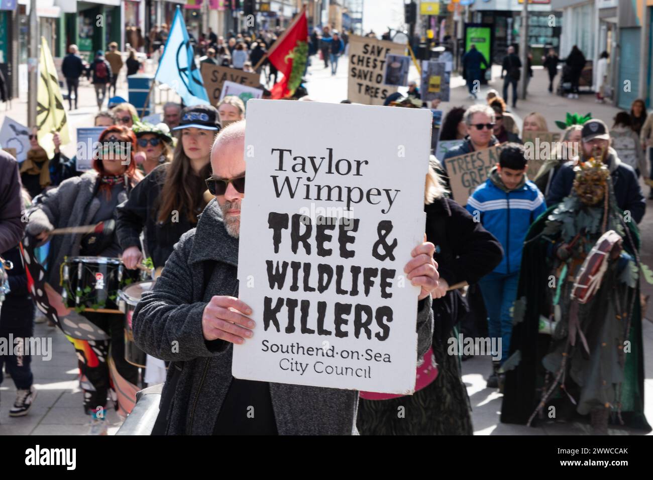 High Street, Southend on Sea, Essex, Regno Unito. 23 marzo 2024. I manifestanti stanno marciando attraverso l'alta Steet fino agli uffici del Consiglio di Southend on Sea, dimostrando contro i piani per abbattere un antico albero della città. Organizzati dal Southend Tree Action Group, i manifestanti sperano di salvare l'albero di platano londinese di 150 anni (Platanus x acerifolia) – soprannominato Chester in onore della sua posizione a Chichester Road – da essere abbattuto a causa della quantità di spazio sul marciapiede che sta occupando vicino a un affollato incrocio stradale e adiacente a un possibile sviluppo abitativo. Cartello di Taylor Wimpey Foto Stock