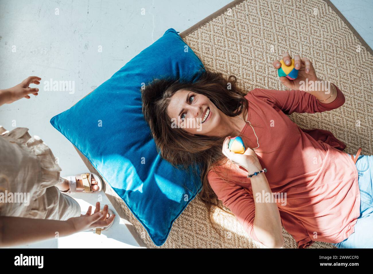Donna sorridente che tiene le palle e si sdraia sul tappeto vicino alla figlia a casa Foto Stock