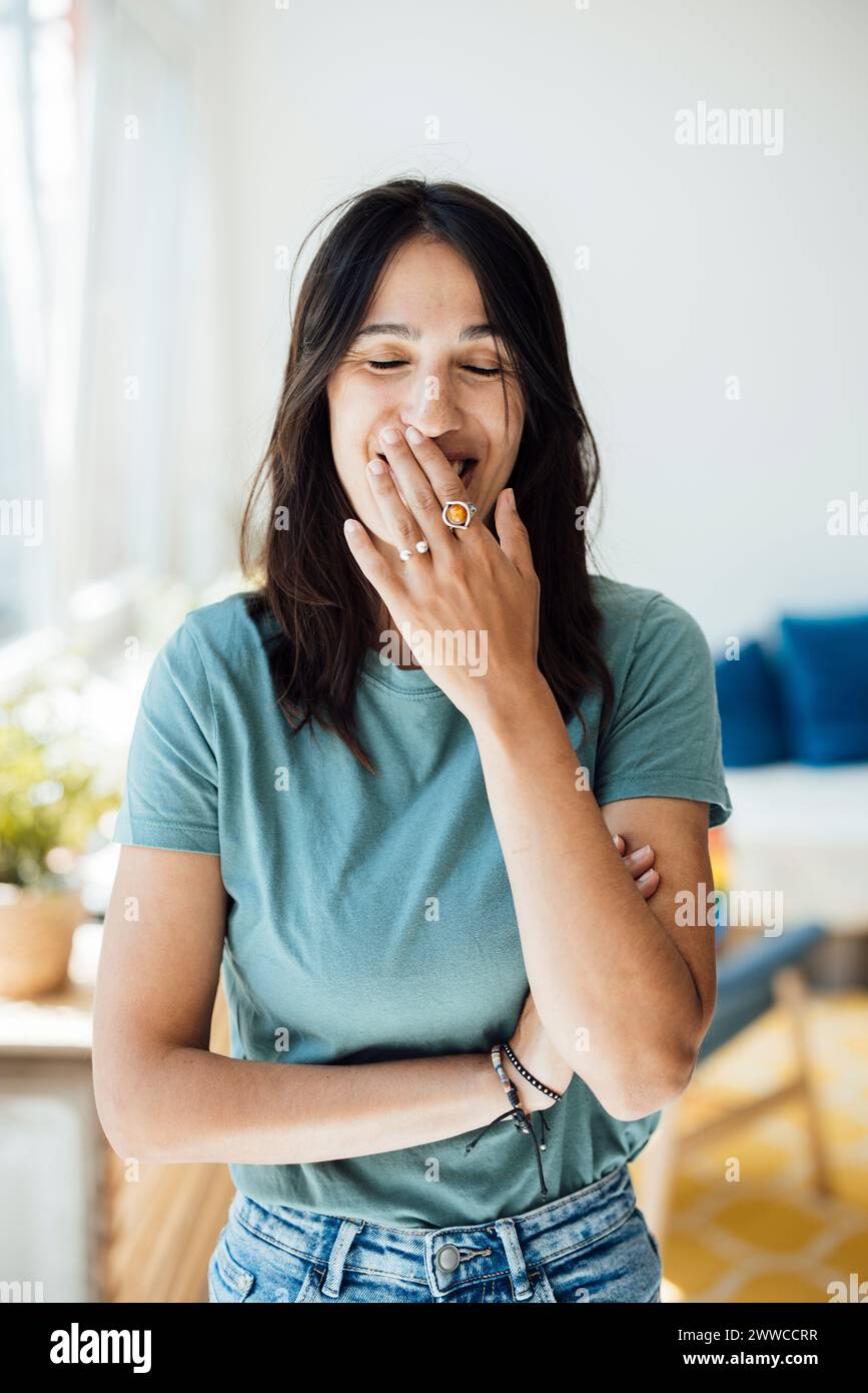 Donna felice con gli occhi chiusi che coprono la bocca a casa Foto Stock