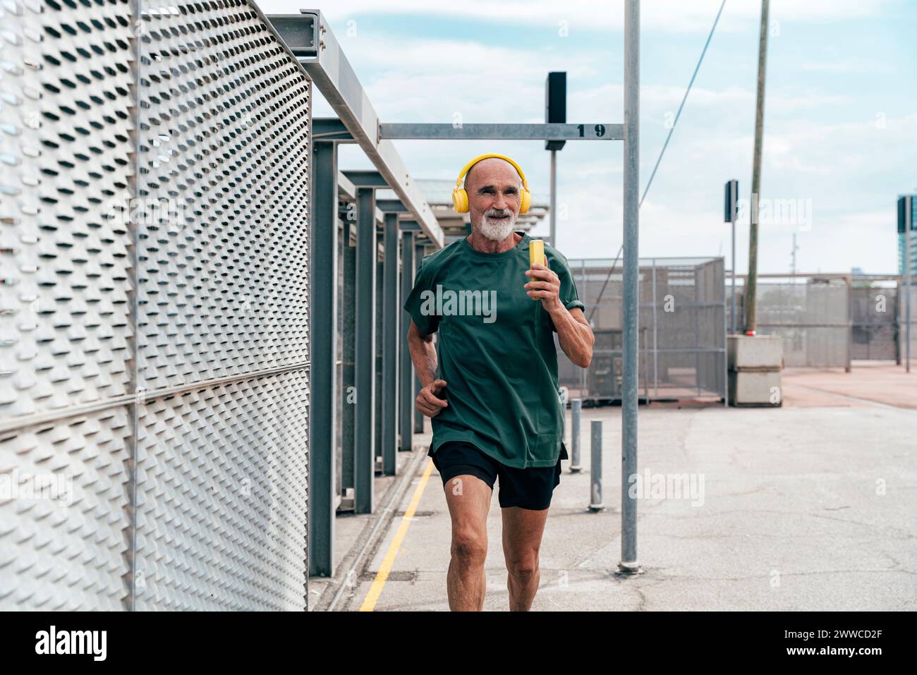 Uomo anziano che ascolta musica e fa jogging per recinzione Foto Stock
