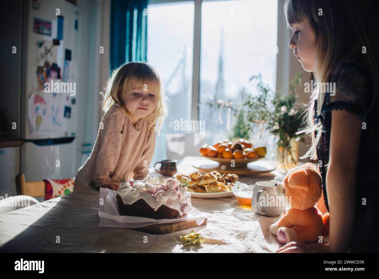 Sorelle che si appoggiano e guardano la torta sul tavolo in cucina Foto Stock