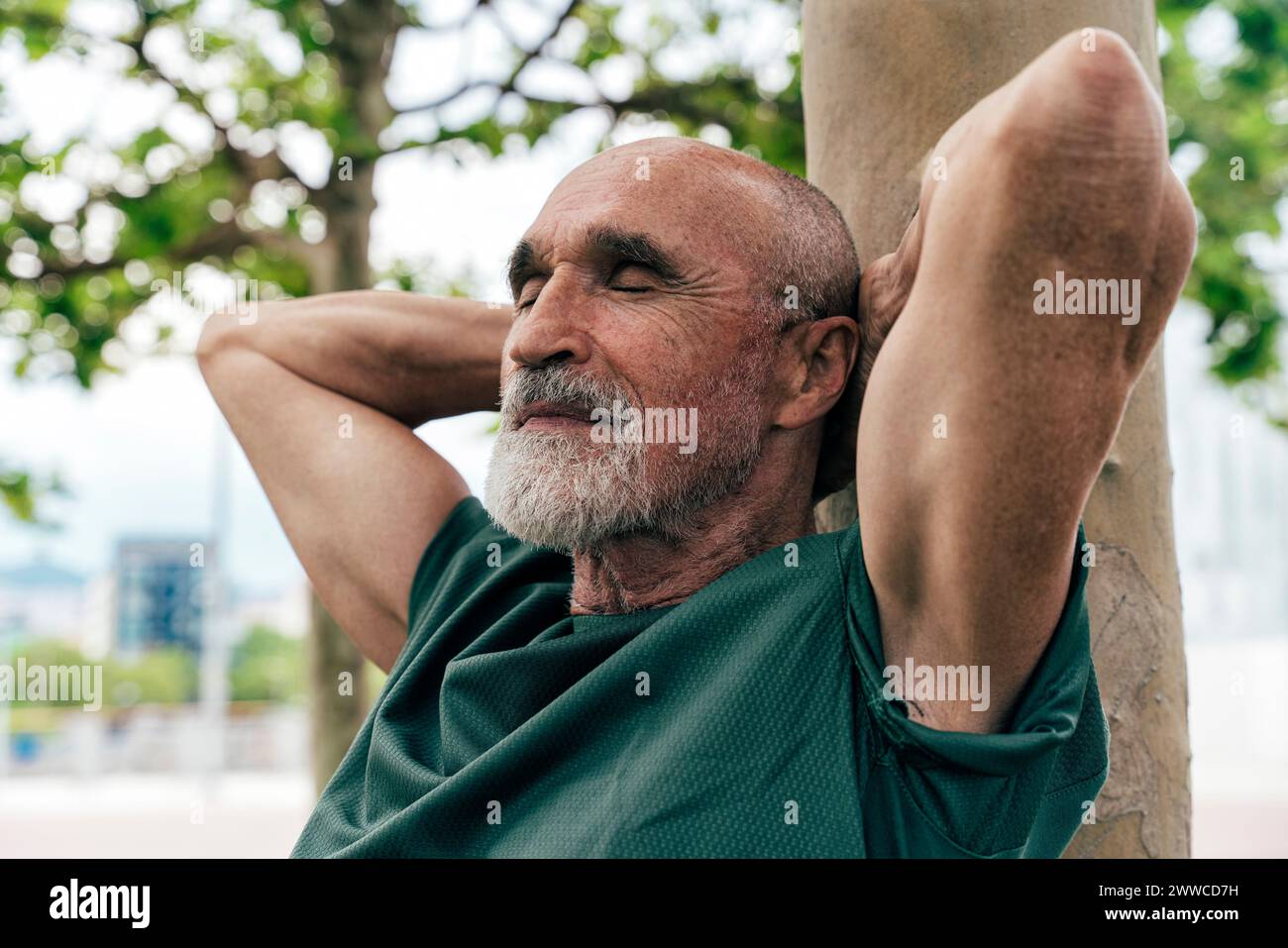 Anziano in pensione appoggiato al tronco dell'albero con gli occhi chiusi Foto Stock