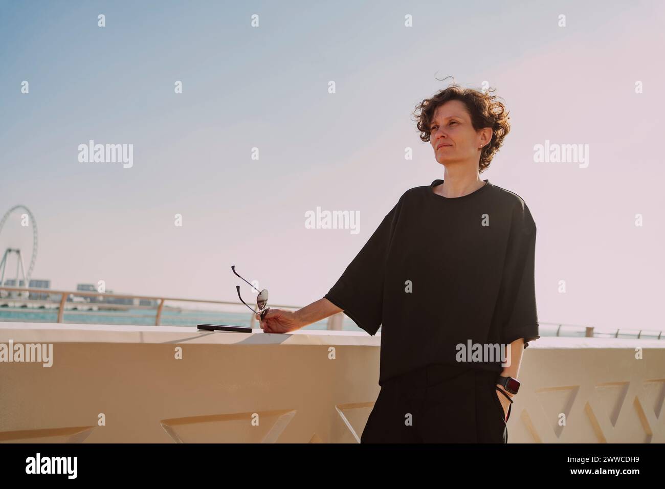 Donna matura in t-shirt nera con occhiali da sole a parete nelle giornate di sole Foto Stock