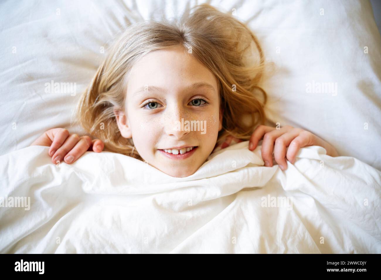 Ragazza sorridente sdraiata a letto con coperta a casa Foto Stock