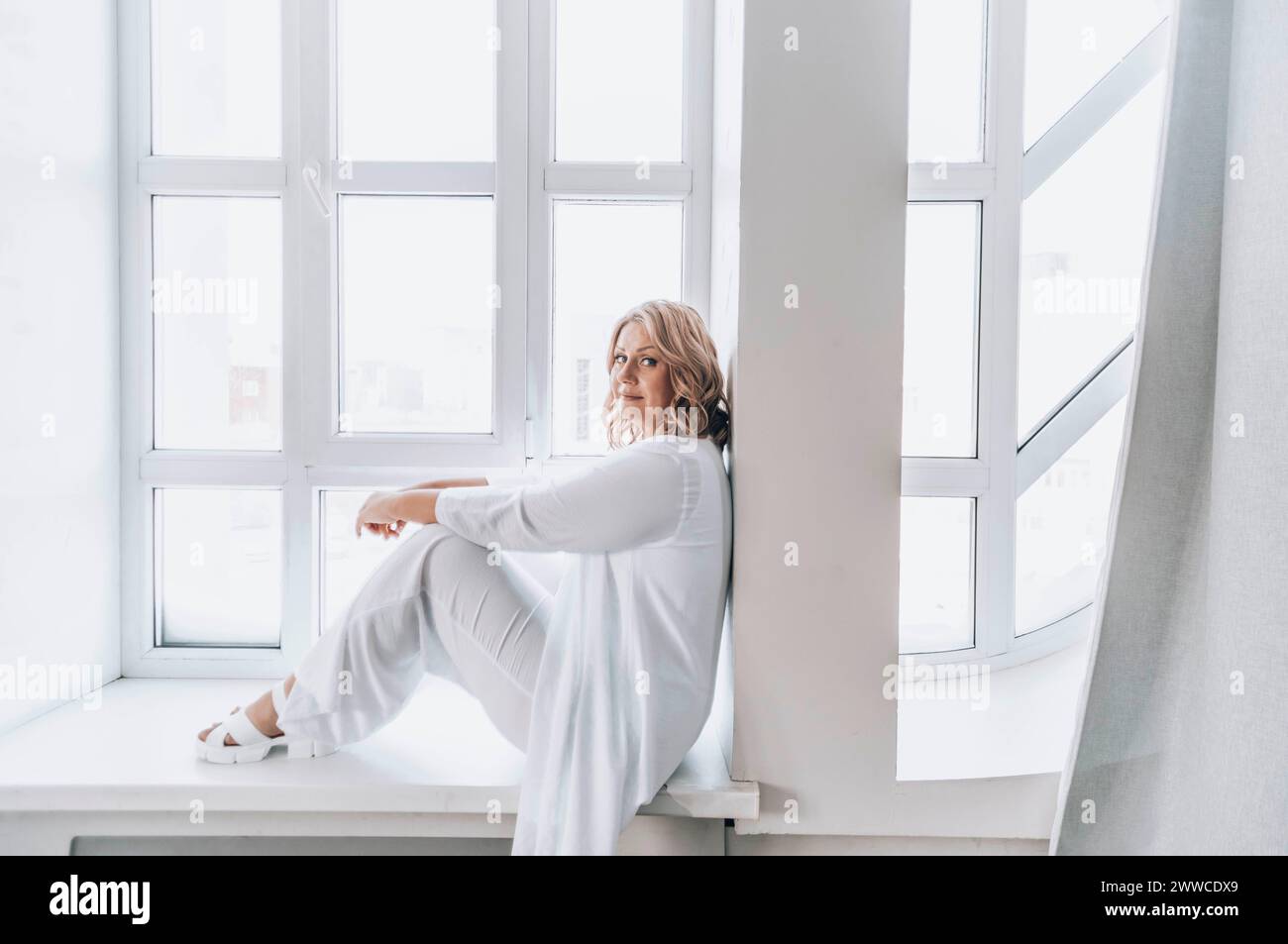 Donna matura seduta sul davanzale a casa Foto Stock