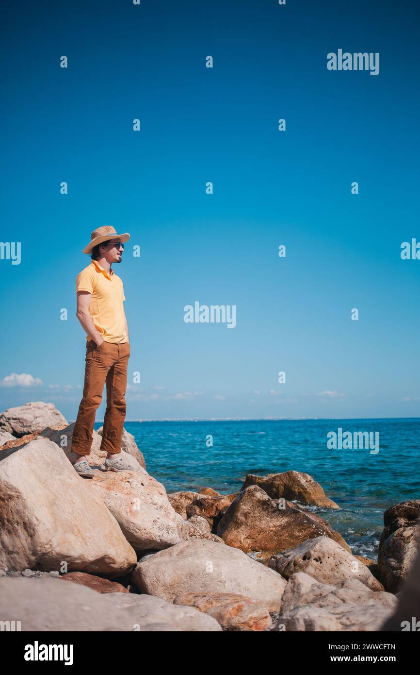 Uomo che trasuda stile contro il mare e che apprezza il viaggio in mezzo alla tranquillità costiera. Foto Stock