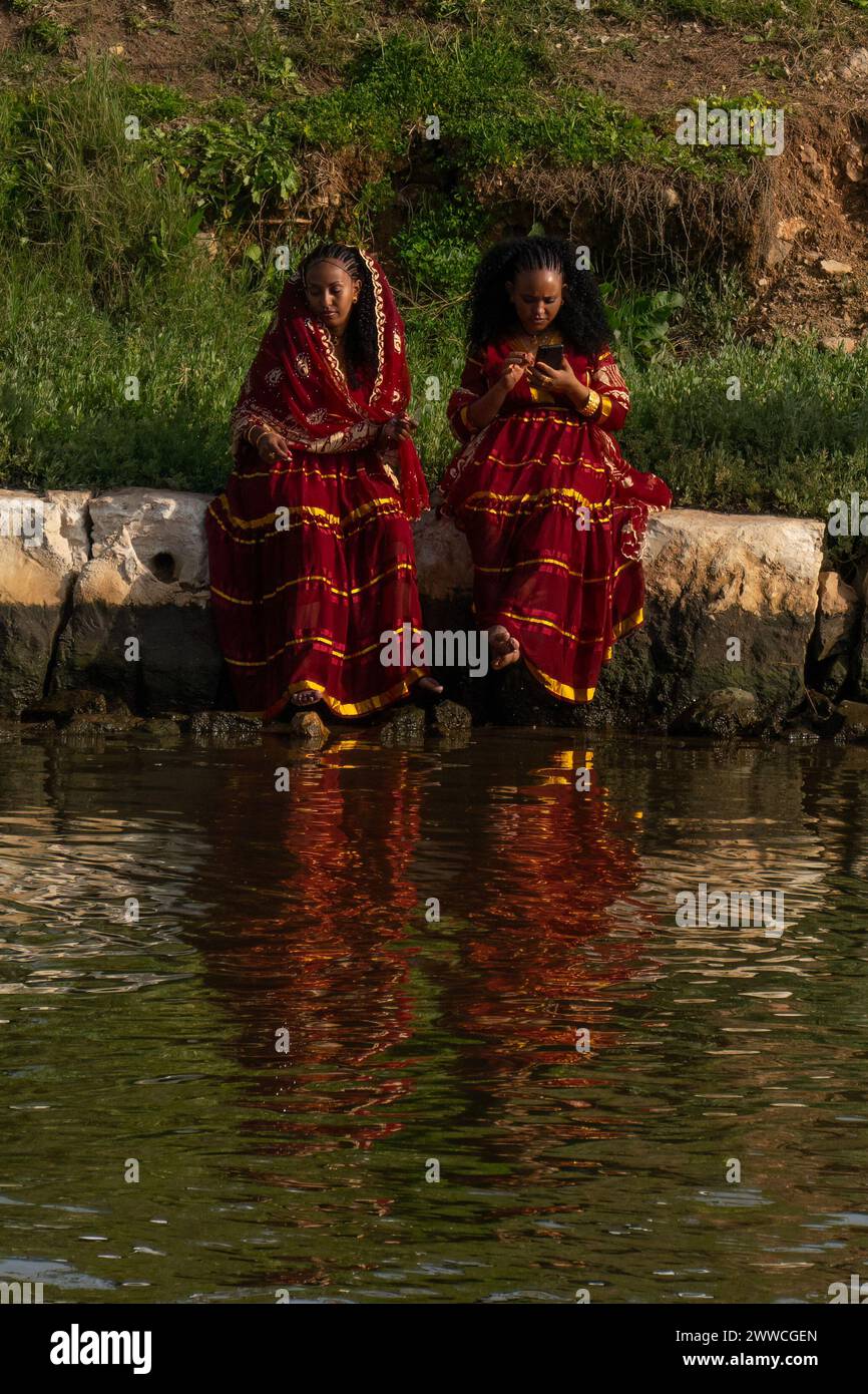Tel Aviv, Israele - 6 gennaio 2023: Due donne di origine africana, che indossano abiti tradizionali festivi, sedute sulla riva del fiume Yarkon. Foto Stock