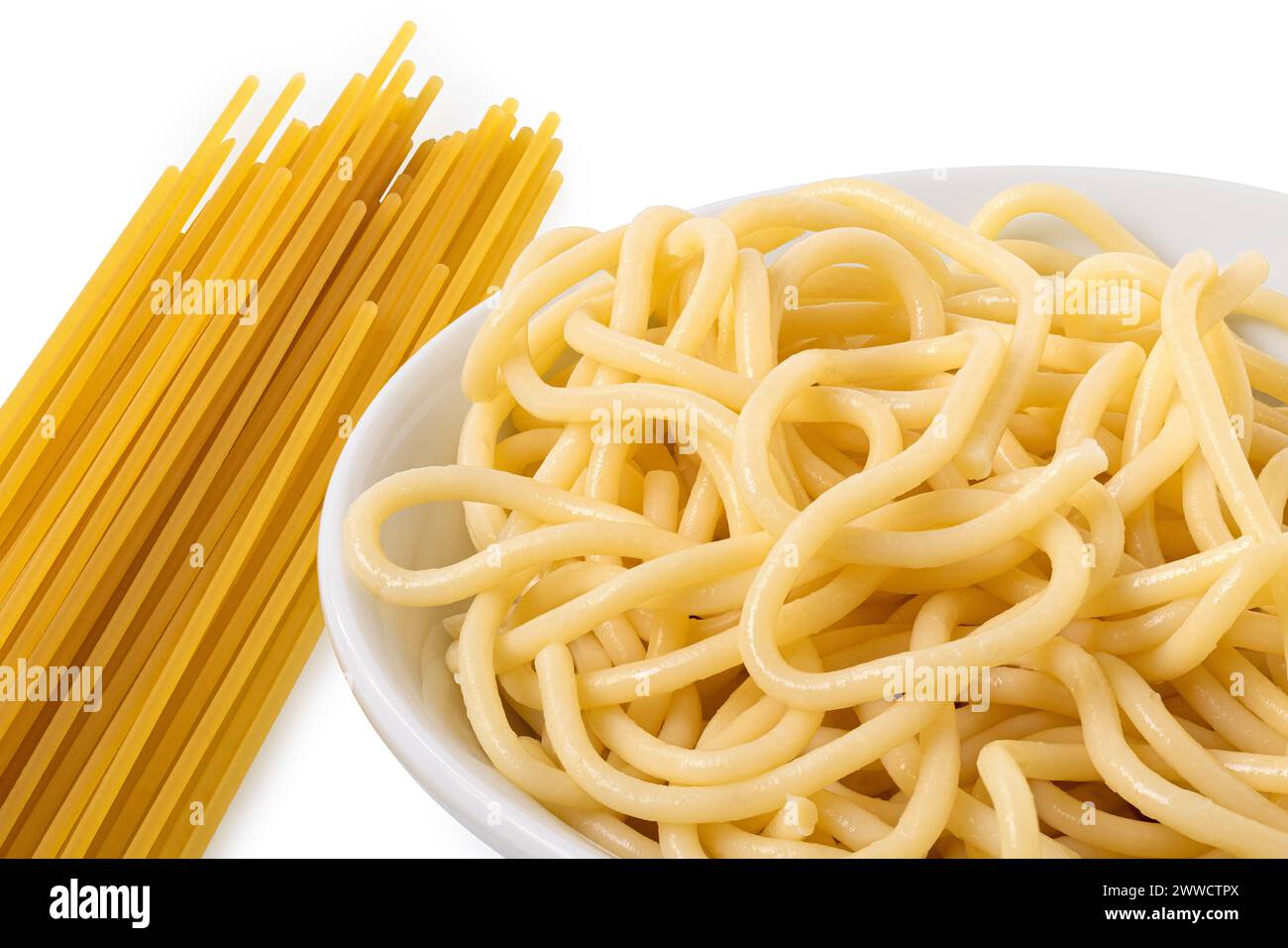 Dettagli degli spaghetti cotti in una ciotola di ceramica bianca accanto agli spaghetti crudi su bianco. Foto Stock