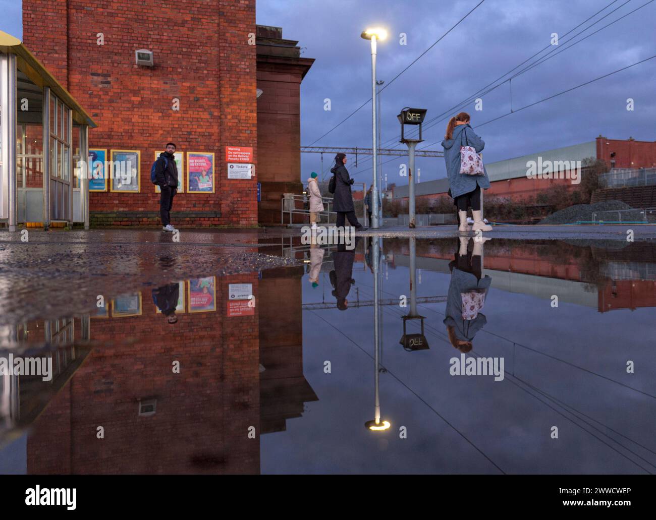 Stazione ferroviaria di Edge Hill, passeggeri in attesa di un treno Northern Rail che si riflette in una pozzanghera sulla piattaforma della stazione Foto Stock