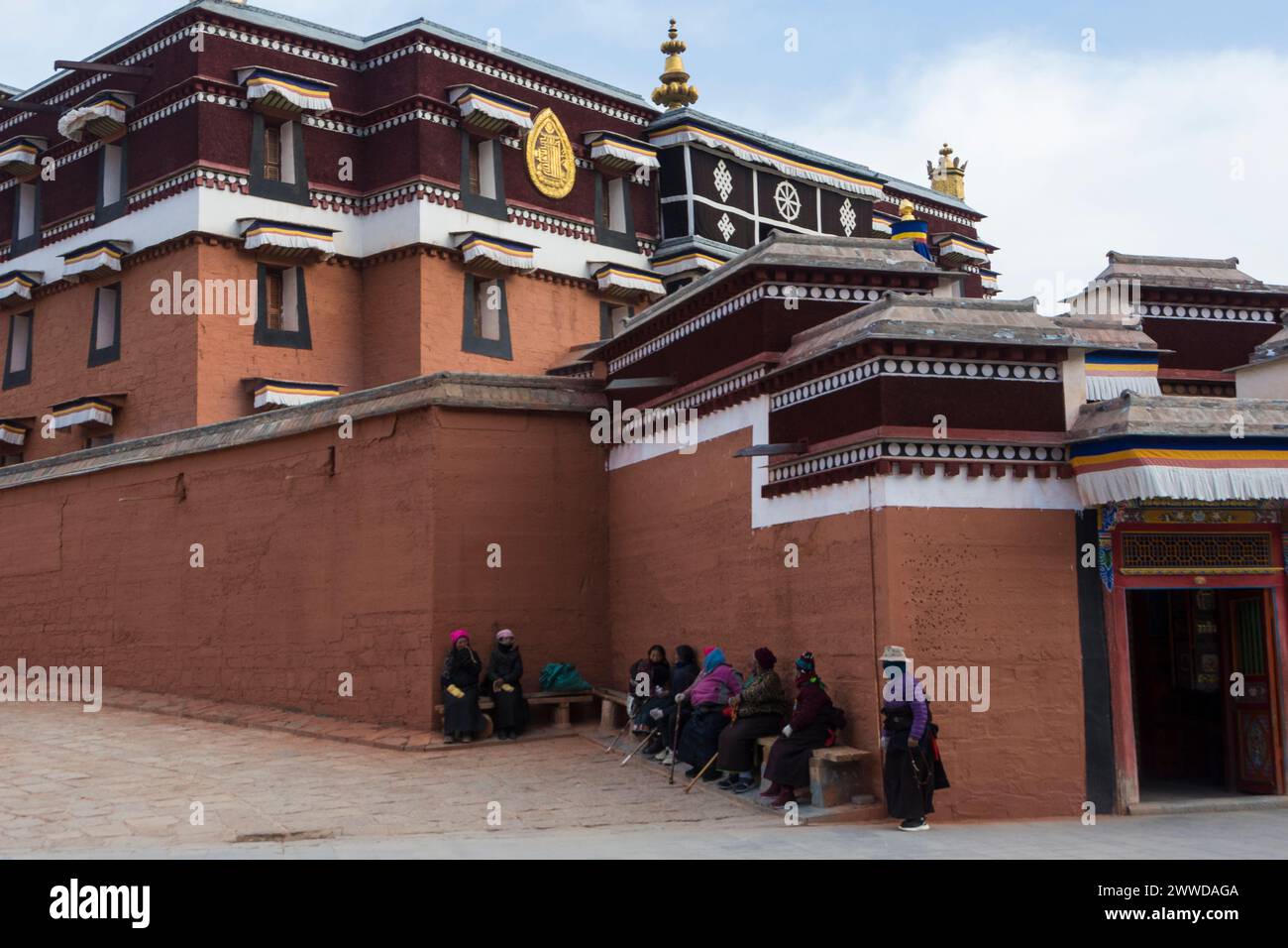 Pellegrini che si riposano su una panchina accanto a uno dei templi del monastero di Labrang, contea di Xiahe, prefettura autonoma tibetana di Gannan, Gansu, Cina Foto Stock