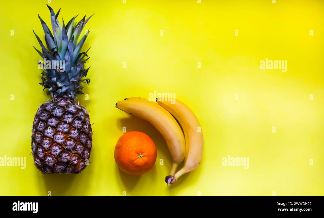 frutta tropicale fresca: banana, arancia, ananas su sfondo giallo. Foto Stock