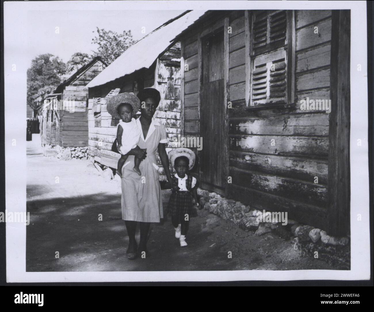 Descrizione: Barbados. Una donna delle Barbadie e i suoi due figli lasciano la loro casa in una zona sovraffollata di Bridgetown. Fotografia n. D 76957 Fotografia ufficiale delle Barbados compilata dall'Ufficio centrale delle informazioni. Luogo: Barbados Data: 1955 Mar barbados, caraibi, caribbeanthrough alens Foto Stock
