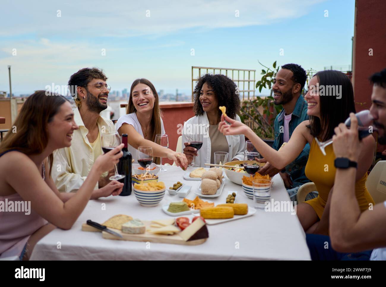 Gruppo ridendo di diversi giovani amici gustando il pranzo insieme all'aperto celebrando la festa sul tetto. Foto Stock