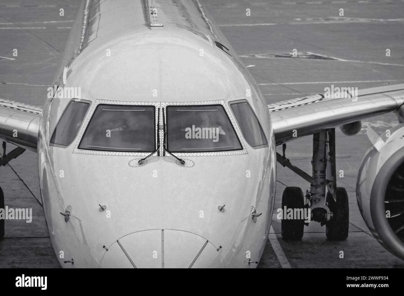 Vista frontale del moderno aereo di linea jet bianco con vista ravvicinata delle finestre della cabina di pilotaggio. L'aereo è seduto su un asfalto in cemento con linee di corsia dipinte. Nero e. Foto Stock