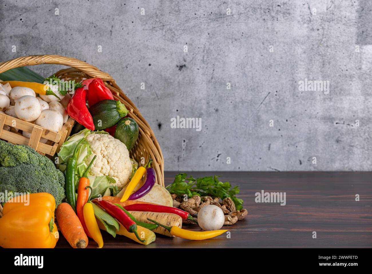 Varie verdure fresche come peperoni, cavolfiore, peperoni, funghi e broccoli in un cesto su una superficie di legno Foto Stock